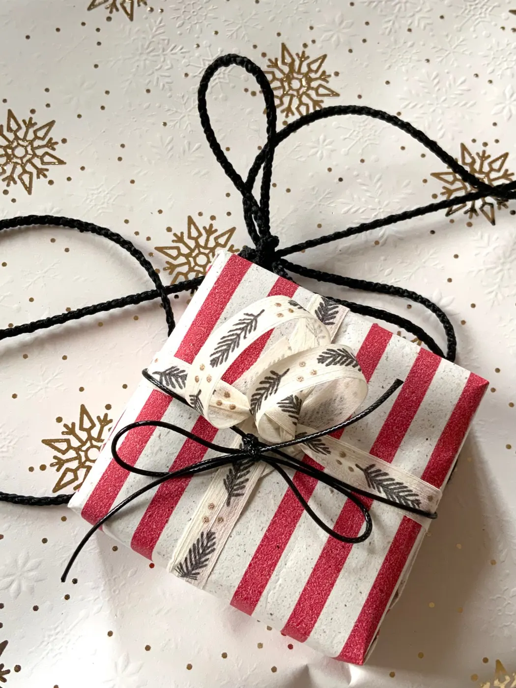 Paquet cadeau emballé dans un papier rayé rouge et blanc, fermé par une ficelle noire