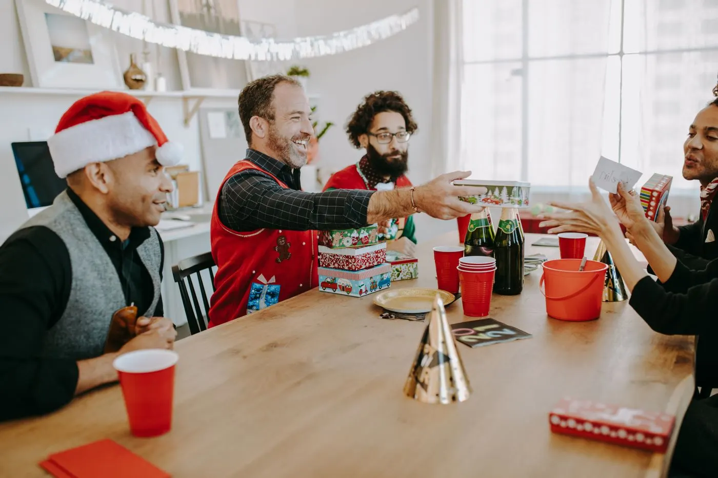 Groupe d'amis en bonnets de Noël autour d'une table, en train de s'échanger des cadeaux