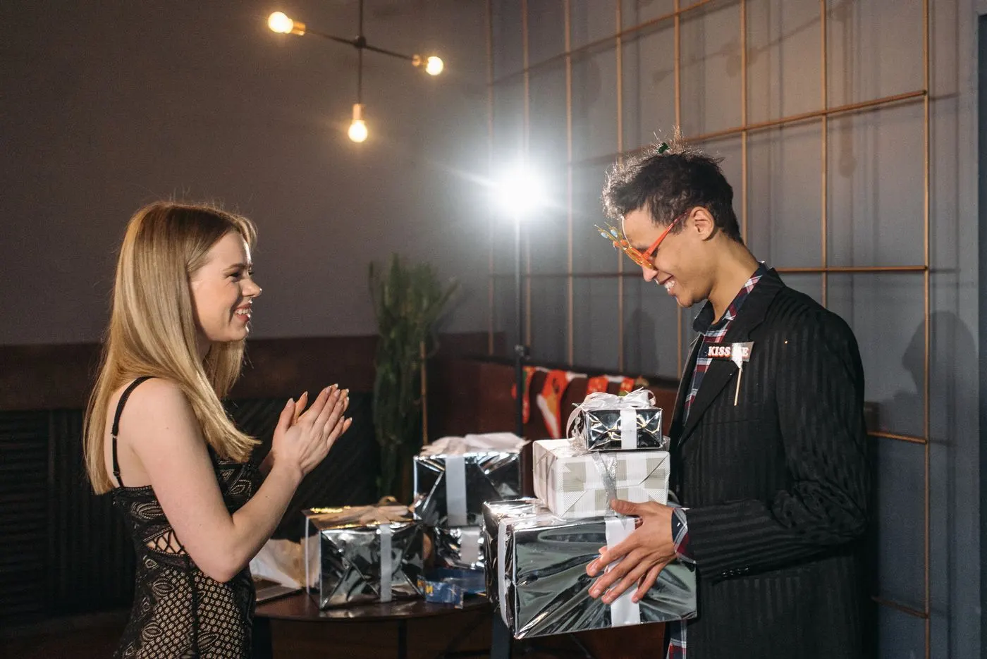 Un homme tient une pile de cadeaux emballés devant une femme qui applaudit