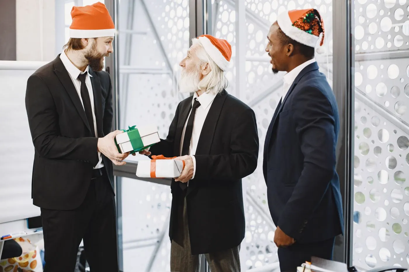 Trois hommes en costume et bonnet de Père Noël échangent des cadeaux